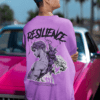 Model wearing a purple oversized sweatshirt with resilience graphic artwork on the back, styled with a vintage pink car outdoors.