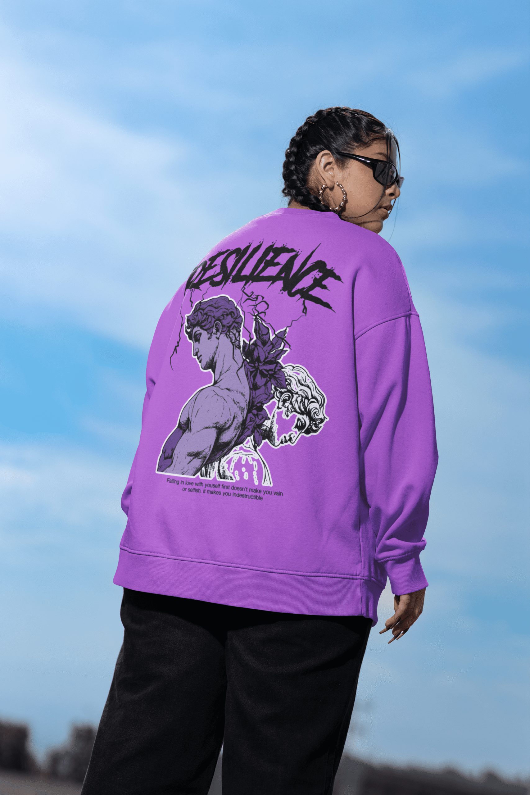 Model wearing a purple oversized sweatshirt with bold resilience graphic artwork on the back, styled outdoors.
