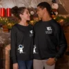 Matching Astronaut Sweatshirts – Dream Big Like the Universe | Leversi Couple wearing matching black astronaut sweatshirts by the fireplace