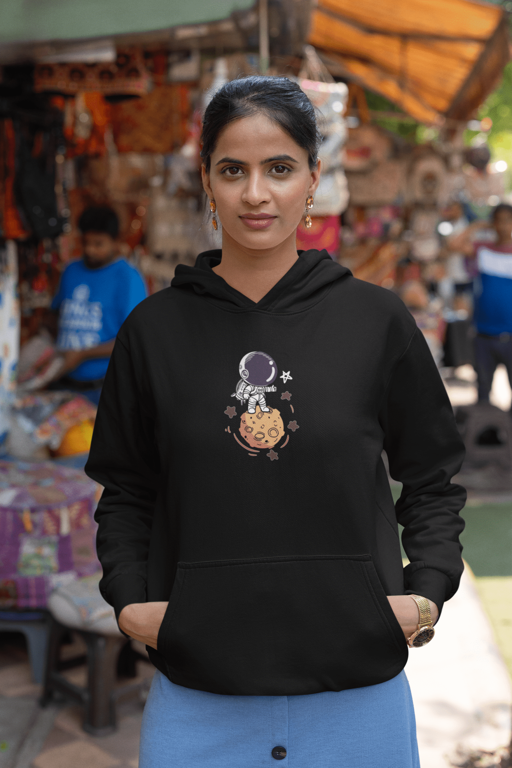 Woman wearing a black astronaut graphic hoodie standing in a colorful street market