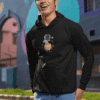 Man wearing a black astronaut graphic hoodie smiling outdoors near colorful street art