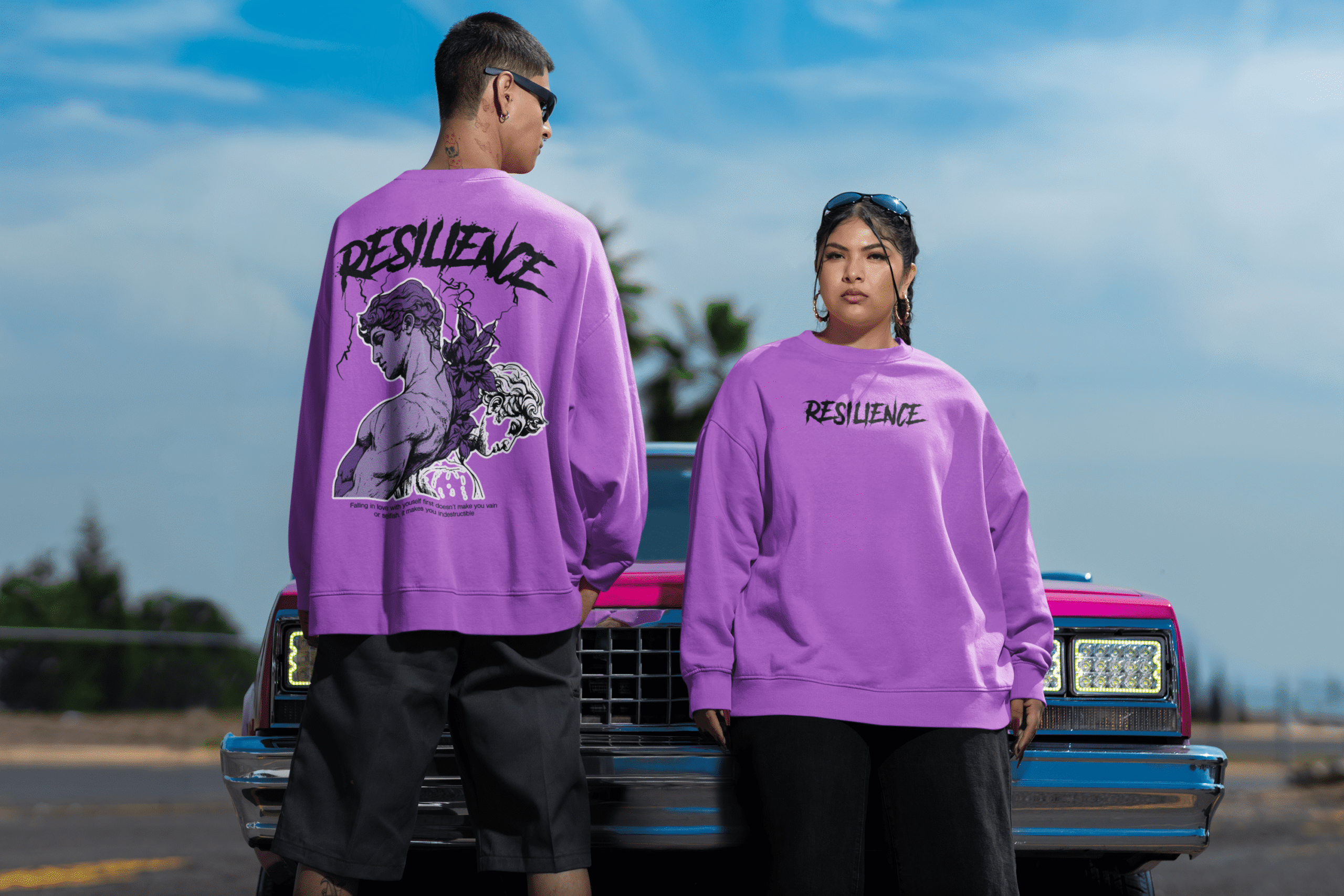 Two models wearing purple oversized resilience sweatshirts showing front and back designs, styled outdoors with a vintage car.