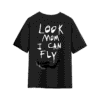 Black oversized T-shirt with large handwritten white text on the back reading “LOOK MOM I CAN FLY,” featuring a small black-and-white graphic of a flying figure near the bottom.