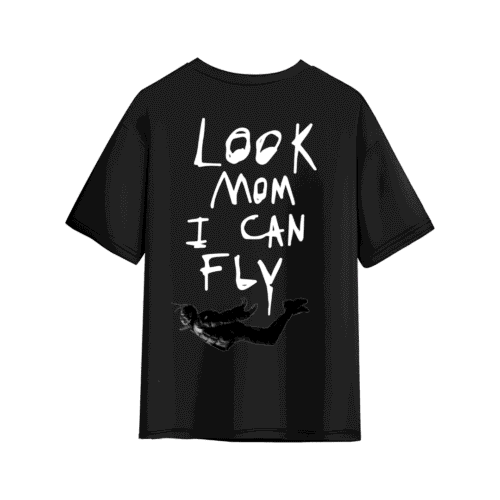 Black oversized T-shirt with large handwritten white text on the back reading “LOOK MOM I CAN FLY,” featuring a small black-and-white graphic of a flying figure near the bottom.