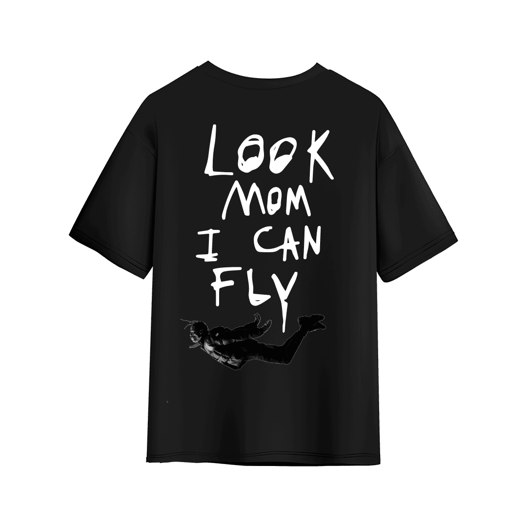 Black oversized T-shirt with large handwritten white text on the back reading “LOOK MOM I CAN FLY,” featuring a small black-and-white graphic of a flying figure near the bottom.