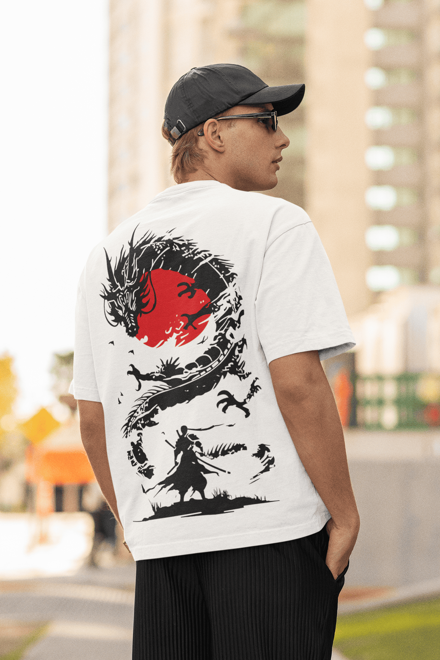 Man wearing a white oversized T-shirt with a black dragon and red sun graphic on the back, standing outdoors in an urban setting.
