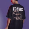 Young man wearing a black oversized T-shirt featuring a large Travis Scott graphic collage on the back, standing under dramatic purple lighting with red highlights.