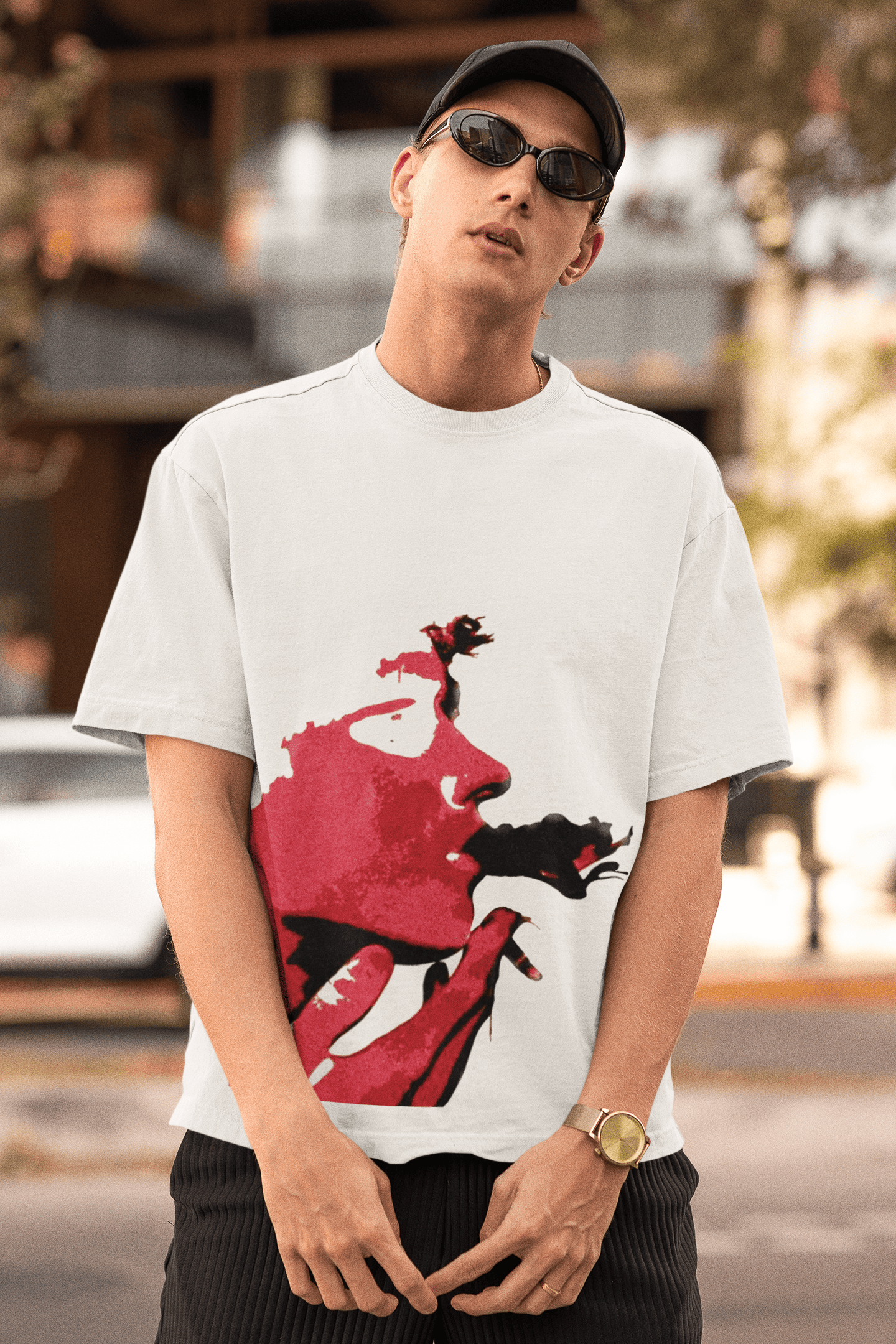 Man wearing white oversized T-shirt with bold red abstract face print while posing outdoors in a relaxed streetwear look.