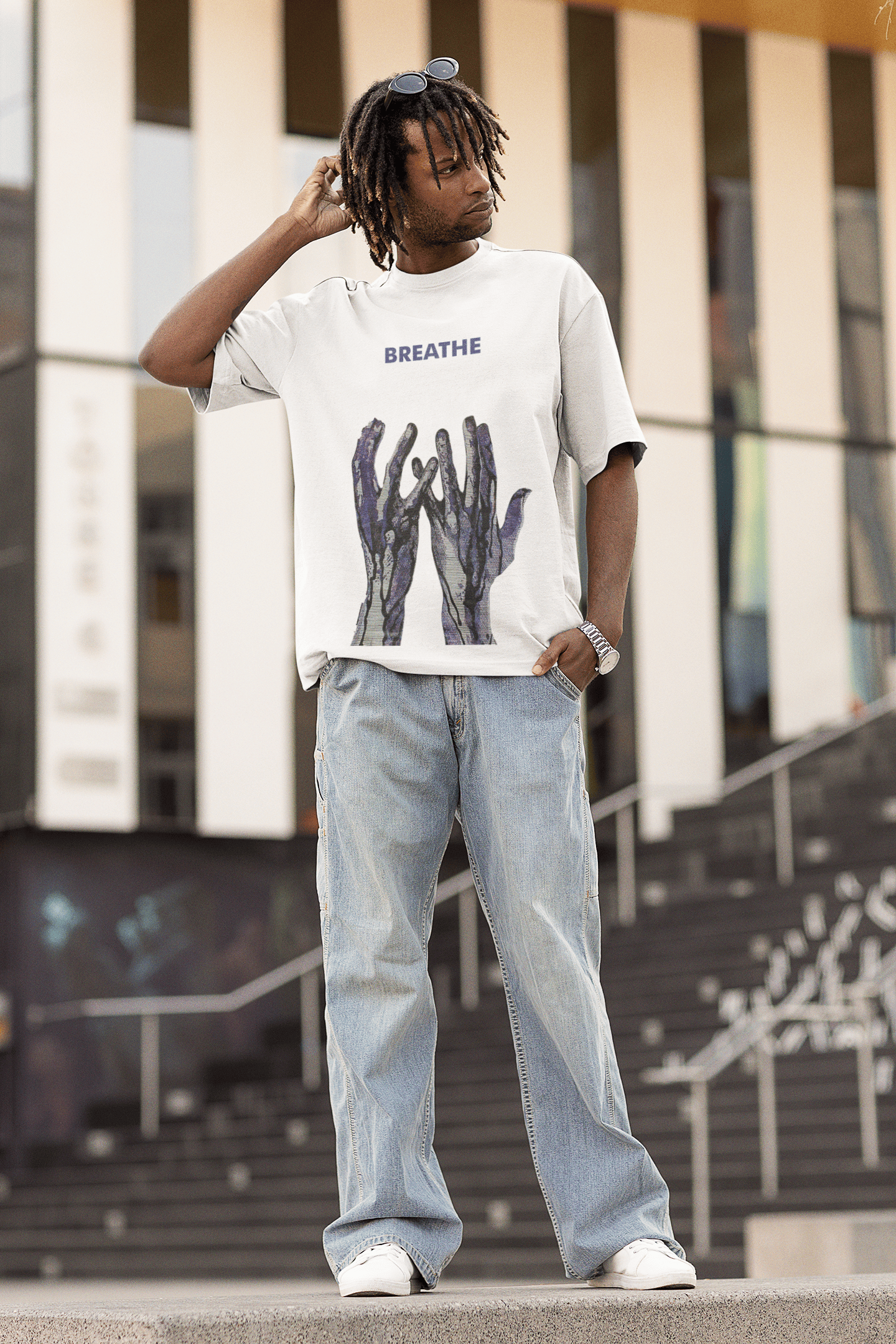 Man wearing a white “BREATHE” graphic T-shirt with abstract blue hand artwork, posing outdoors in relaxed streetwear.