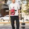 Man wearing white oversized T-shirt with bold red abstract face print while standing outdoors in a street-style setting.