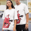 Man and woman wearing matching white graphic T-shirts with bold red face artwork in an outdoor urban setting.