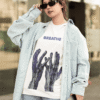 Woman wearing a white “BREATHE” graphic T-shirt with blue abstract hand design, styled with an oversized light denim shirt, jeans, and black sunglasses outdoors.