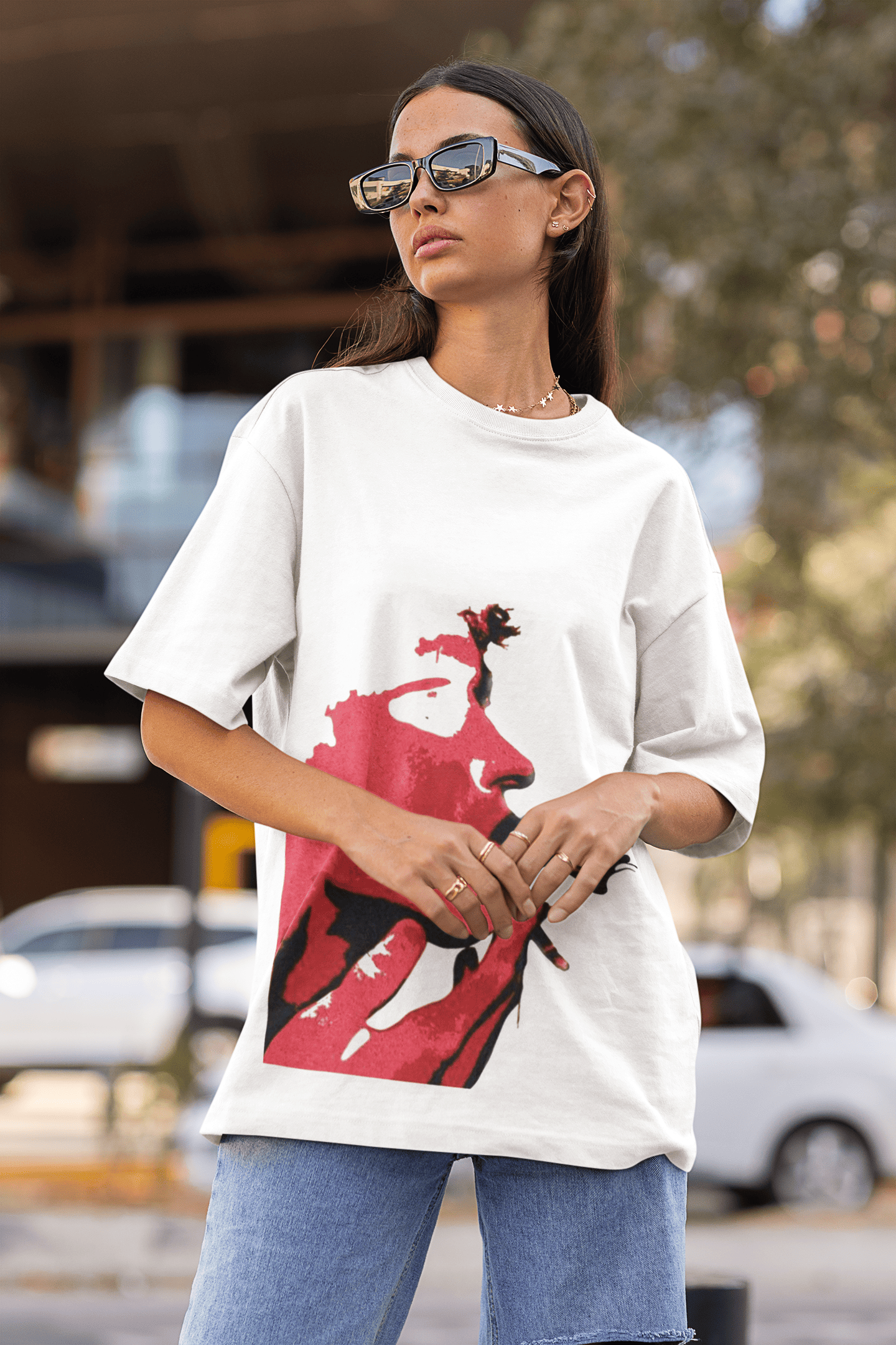 Woman wearing a white oversized T-shirt with a bold red artistic face graphic while posing outdoors in an urban setting.