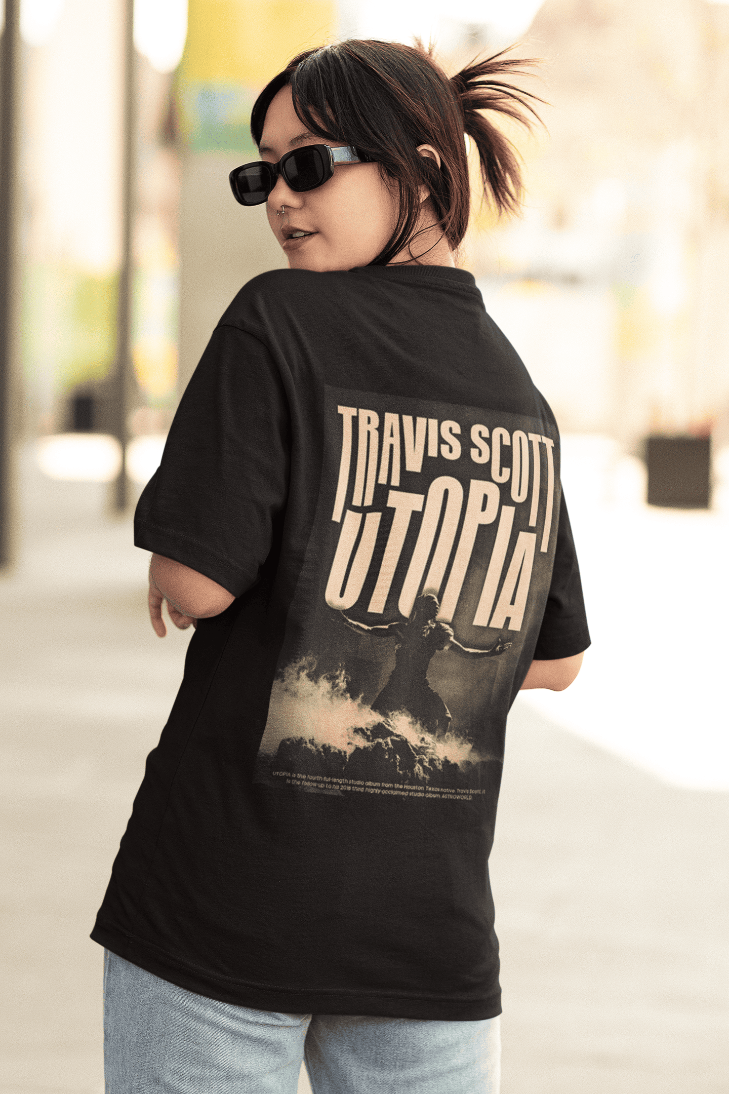 Person wearing a black T-shirt with a large Travis Scott “UTOPIA” back print featuring a dramatic sepia-toned image of a figure standing in rising smoke.
