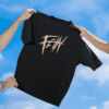 Hands holding up a black T-shirt against a bright blue sky with clouds, featuring a bold beige graffiti-style “FE!N” graphic on the front.