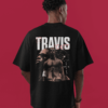Man wearing a black oversized T-shirt with a large graphic on the back featuring multiple artistic portraits of Travis Scott, bold “TRAVIS” text, red detailing, and Cactus Jack–style markings.
