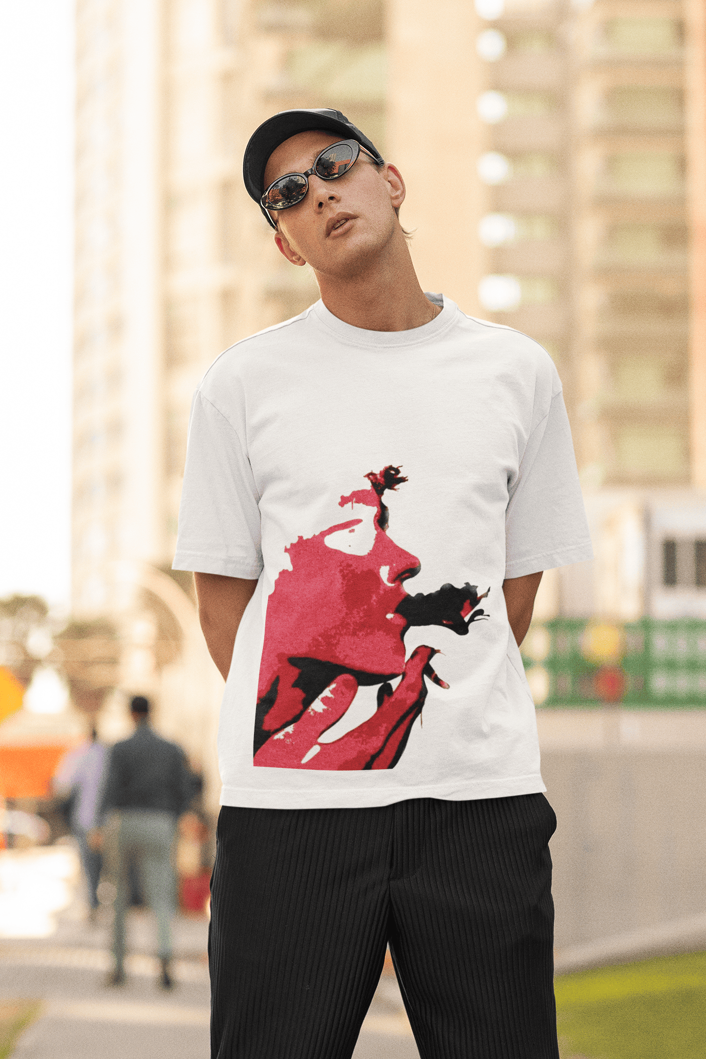 Man wearing a white T-shirt with a bold red artistic face graphic while posing outdoors in an urban setting.