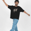 Man posing with arms outstretched while wearing a black oversized T-shirt featuring a bold beige “FE!N” graffiti-style graphic on the front, paired with light blue cargo jeans and white sneakers against a minimal white background.