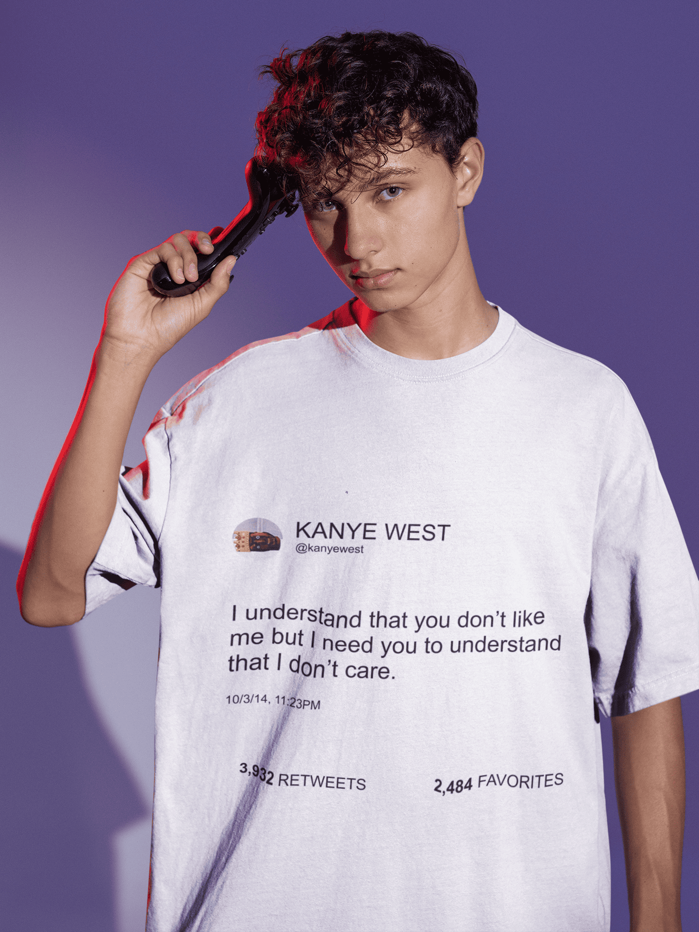 Teenage boy wearing an oversized white Kanye West tweet T-shirt while holding a gaming controller against a purple background.
