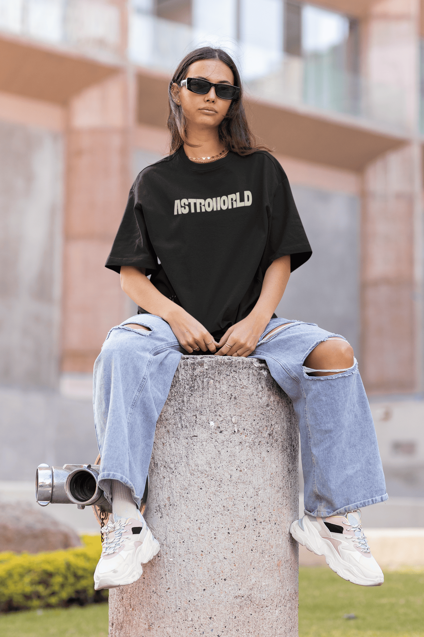 Woman wearing a black Astroworld T-shirt and ripped jeans, sitting outdoors on a concrete block.