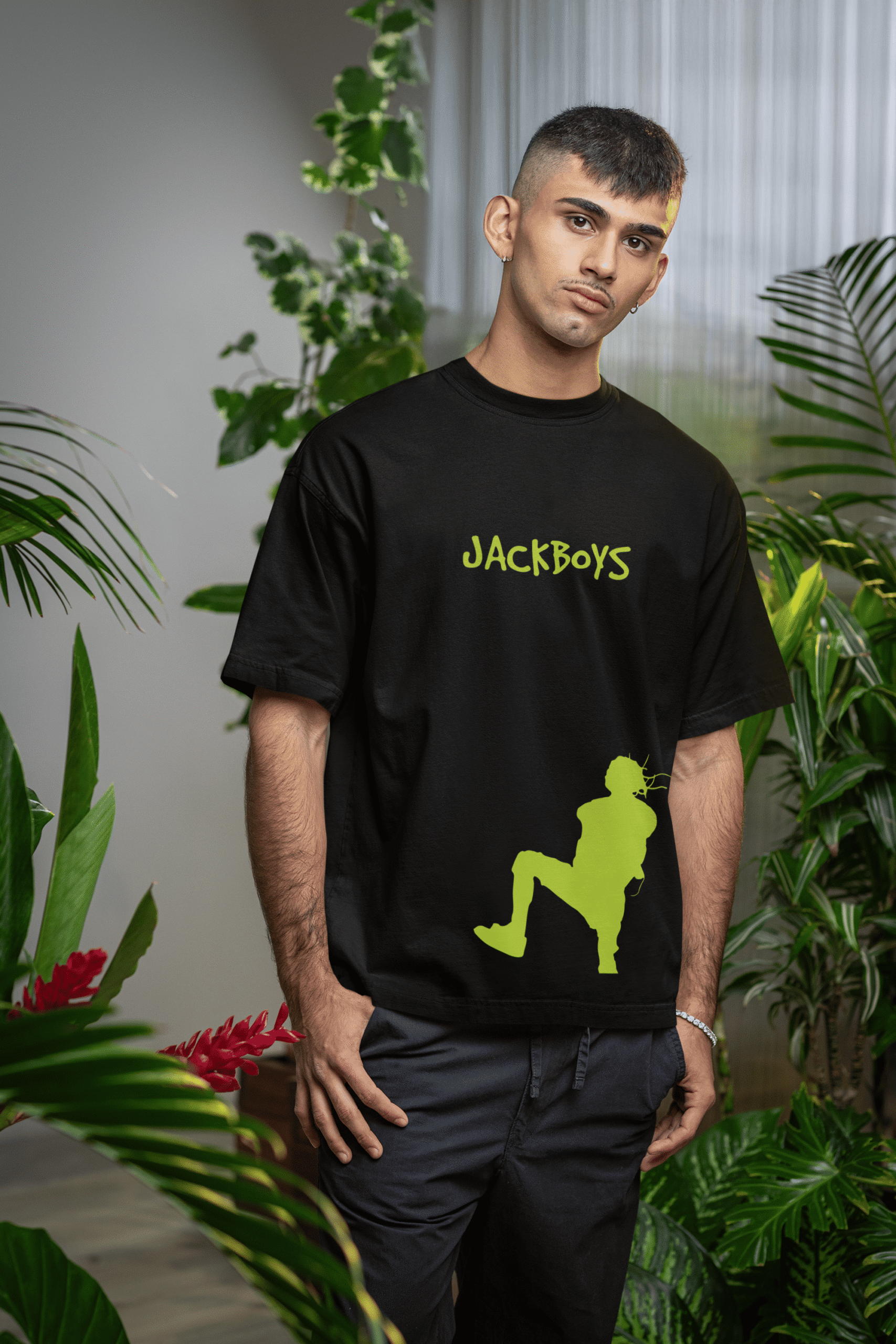 Man wearing a black oversized T-shirt with a neon green JACKBOYS logo on the chest and a bold silhouette graphic near the hem.